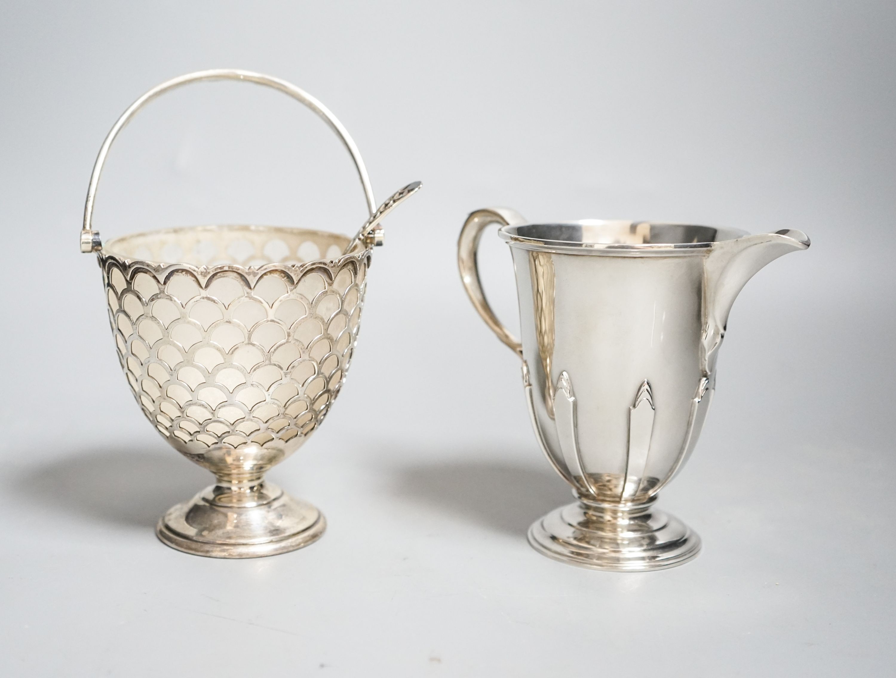A modern silver sugar basket and sifter spoons, with glass liner by Mappin & Webb, 9.8cm and an earlier silver cream jug by William Comyns & Sons Ltd.